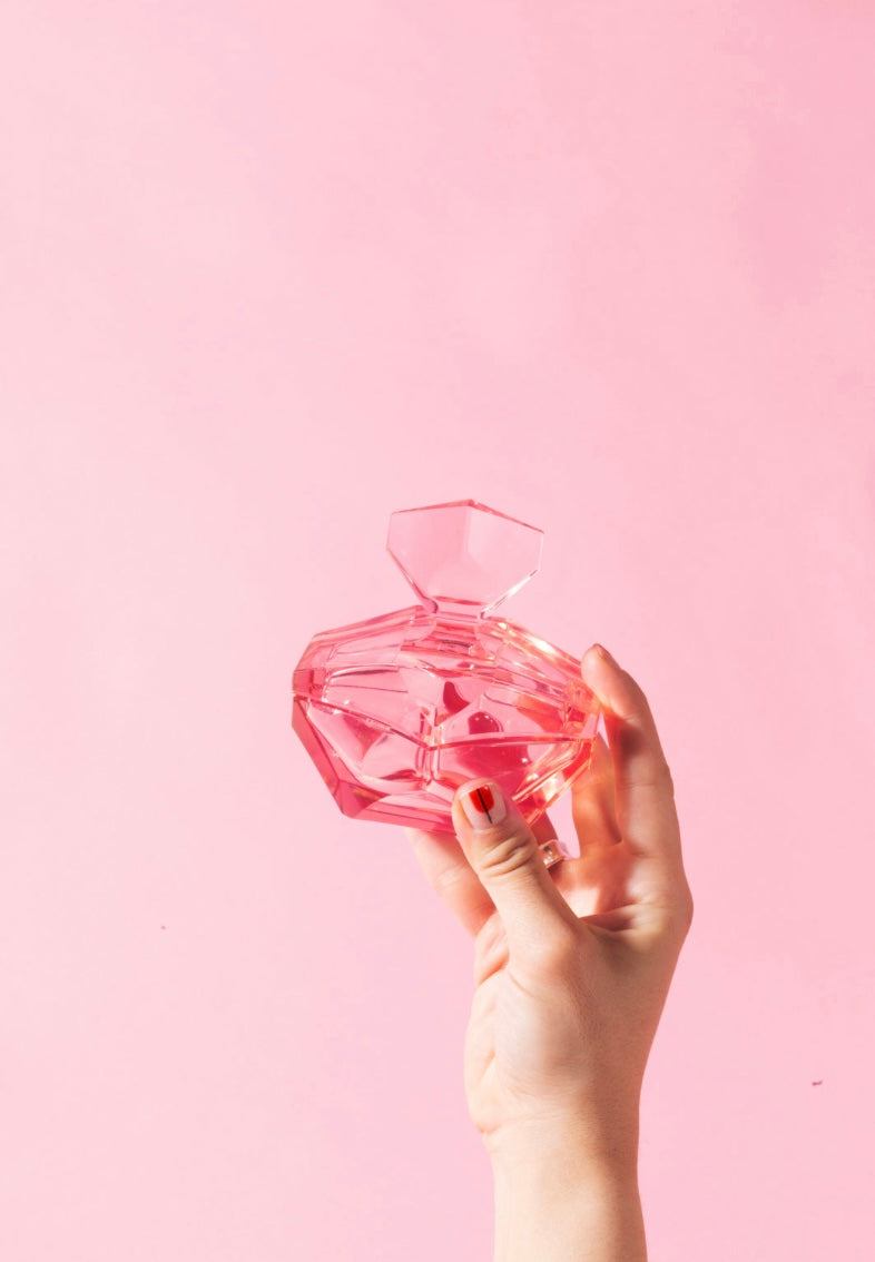 Hand holding a crystal perfume bottle against a pink background