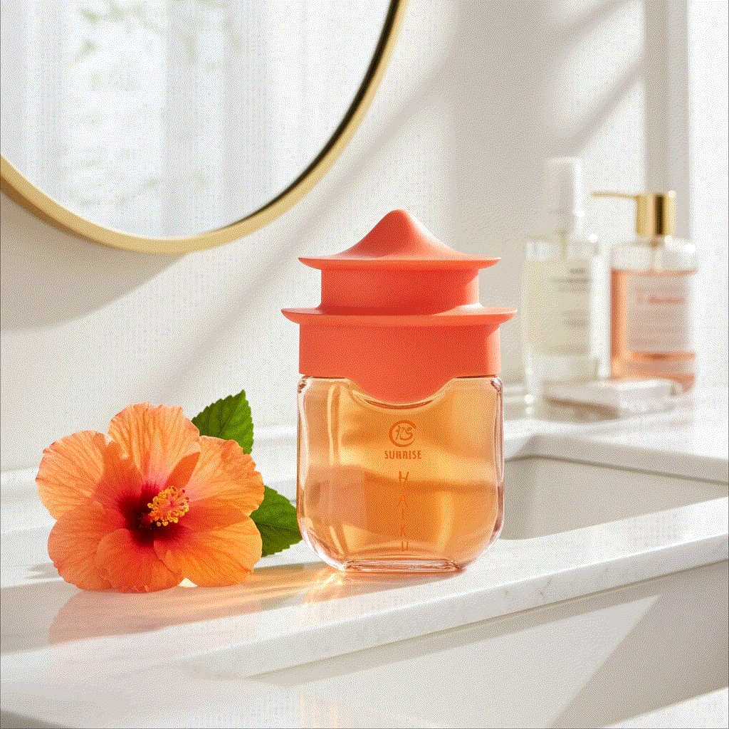 Haiku Sunrise Eau De Perfume bottle with orange cap and hibiscus flower on white bathroom counter with mirror reflection