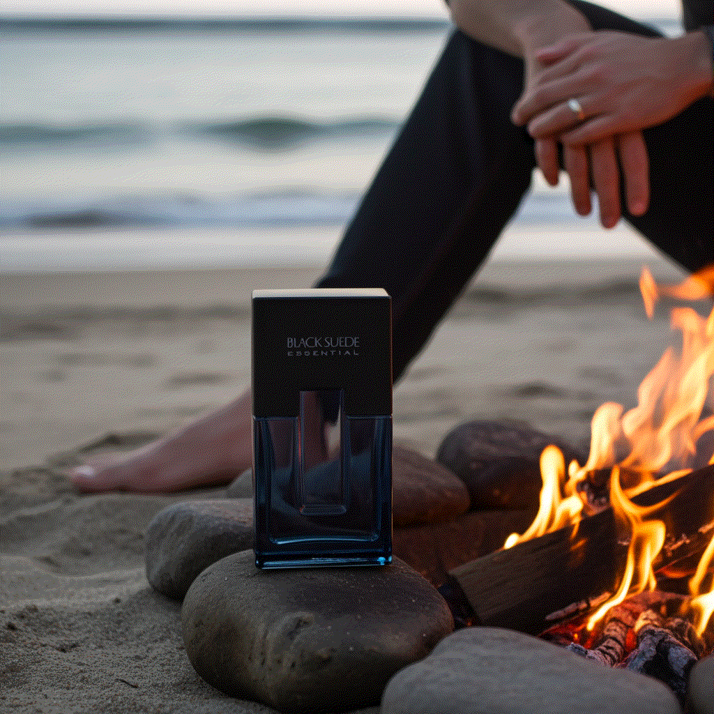 Black Suede Essentials men's cologne bottle on rocks by beach campfire with ocean background
