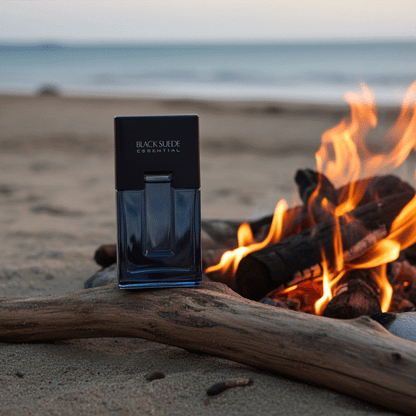 Black Suede Essentials men's cologne bottle on beach near fire with ocean background