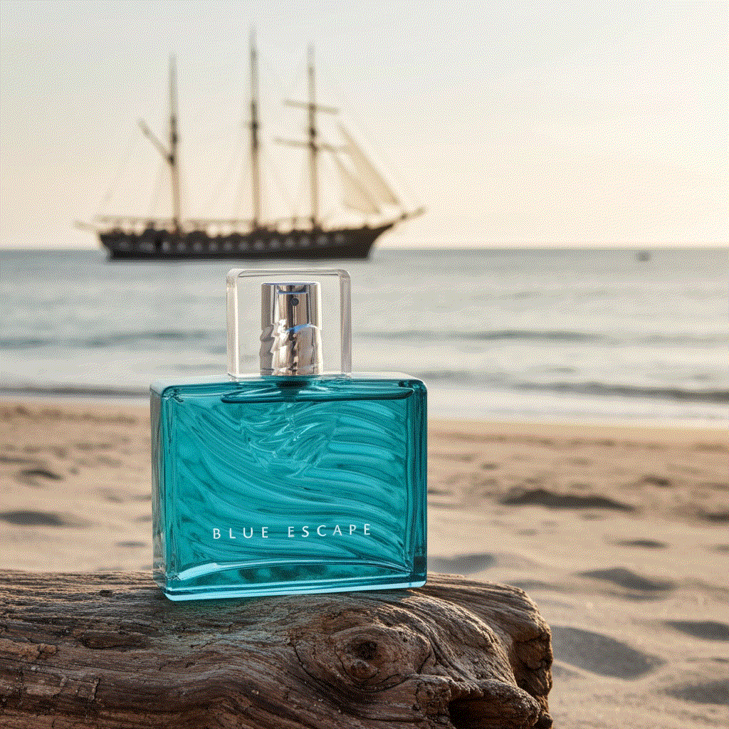 Blue Escape For Him cologne bottle on beach with sailing ship background